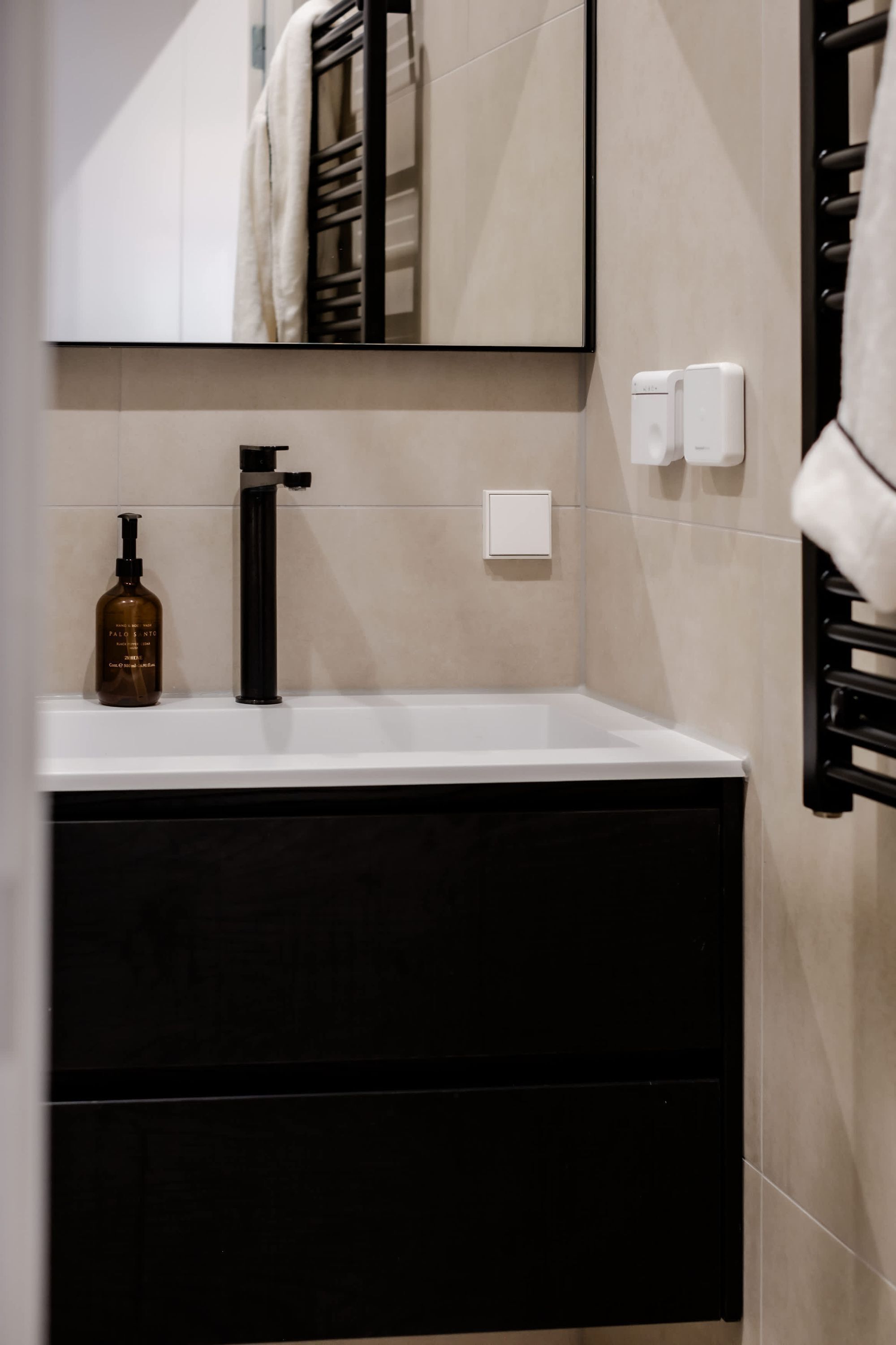 A bathroom with a white sink, black faucet, and a bottle of hand soap.