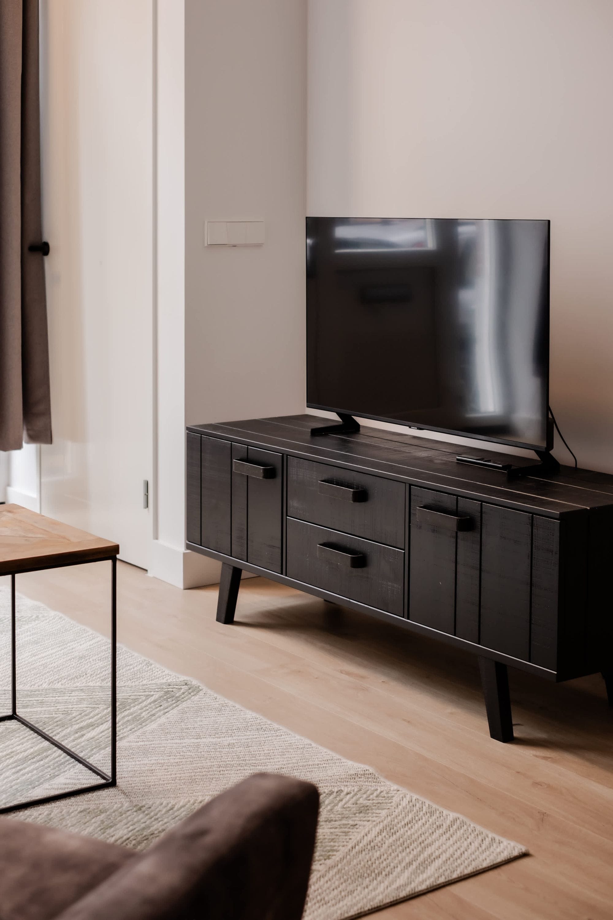 Ett modernt vardagsrum med ett mörkt träskåp, en platt-TV och en ljus matta.