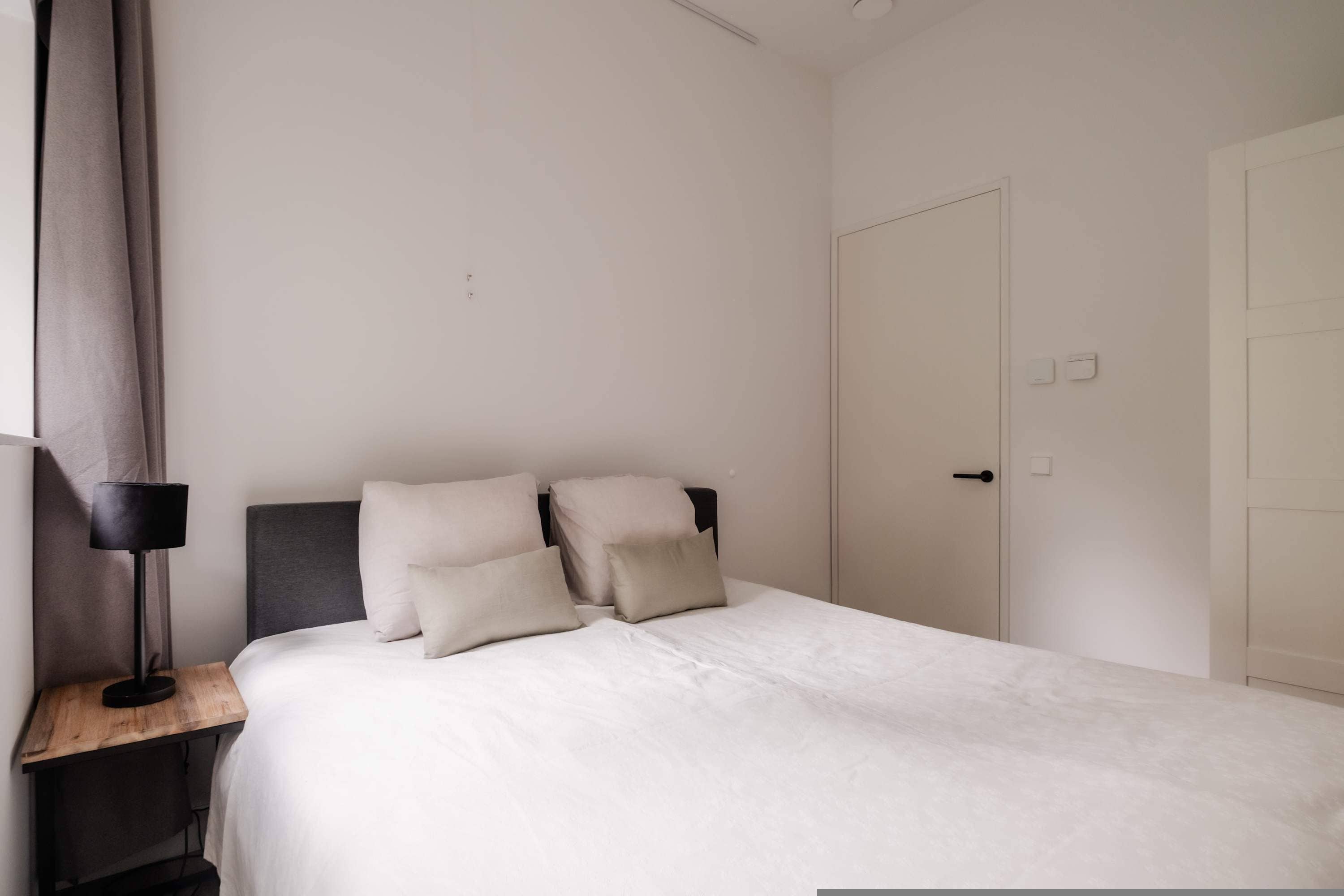 Un dormitorio con cama, mesita de noche, lámpara y puerta.