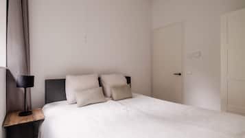 A bedroom with a bed, a nightstand, a lamp, and a door.
