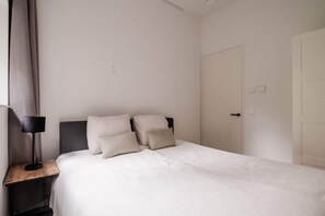 A bedroom with a bed, a nightstand, a lamp, and a door. - Spacious 2BR in Heart of Schiedam (Schiedam)
