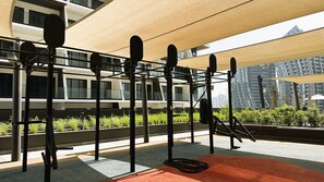 Ein Fitnessbereich im Freien mit Trainingsgeräten, einem roten Teppich und Blick auf eine Stadtlandschaft.
