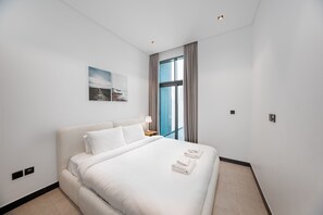 Ett modernt hotellrum med en stor säng, ett nattduksbord, en lampa och ett fönster med gardiner.