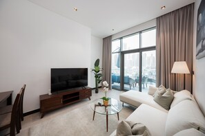 Una sala de estar moderna con un televisor de pantalla plana, un sofá, una mesa de centro y vistas de un paisaje urbano a través de amplios ventanales.