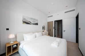 Ein Hotelzimmer mit Bett, Nachttisch, Lampe, Spiegel, Schrank und einer Tür zu einem weiteren Raum.