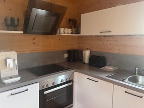 Una cuina compacta amb forn integrat, fogó, cafetera i torradora.