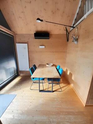 Huoneessa on puinen pöytä, siniset tuolit, valkotaulu ja kattovalaisin.