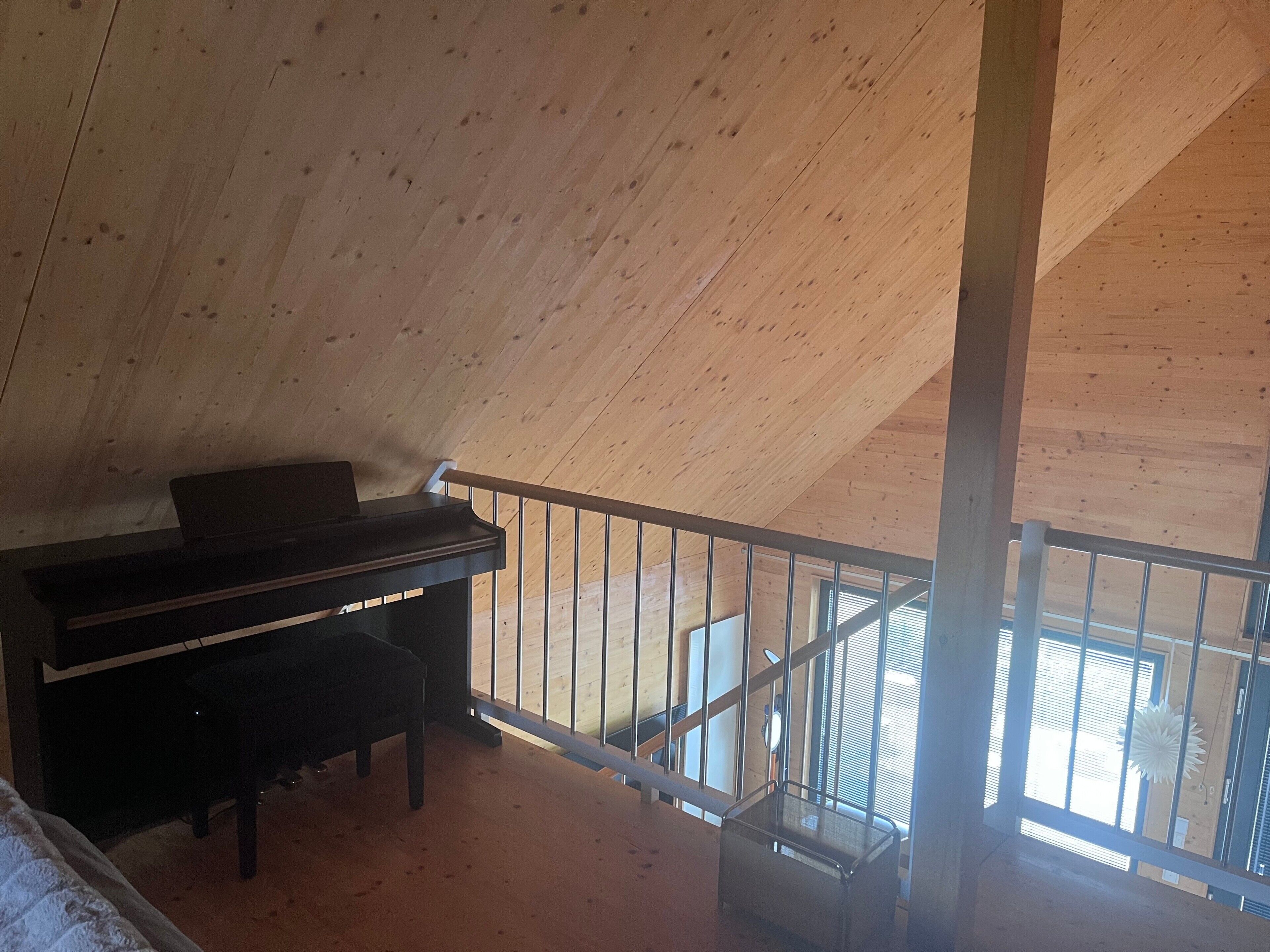A room with a wooden ceiling, a piano, and a view through a window.