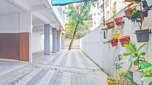 A narrow alleyway with a tiled pavement, a tree in the distance, and potted plants on the right side. - Super Collection O Baner (Pune)