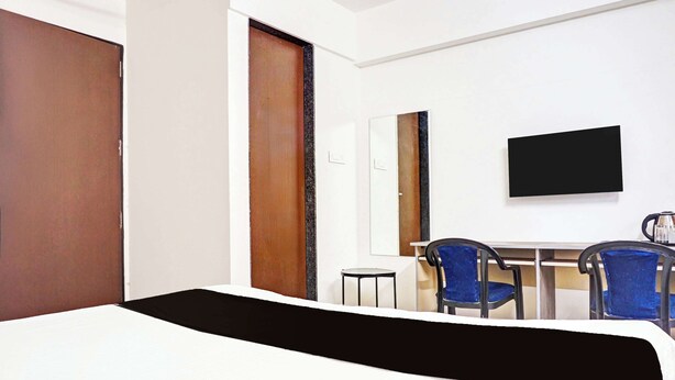 A hotel room with a bed, a desk, two chairs, a television, and a door. - Super Collection O Baner (Pune)