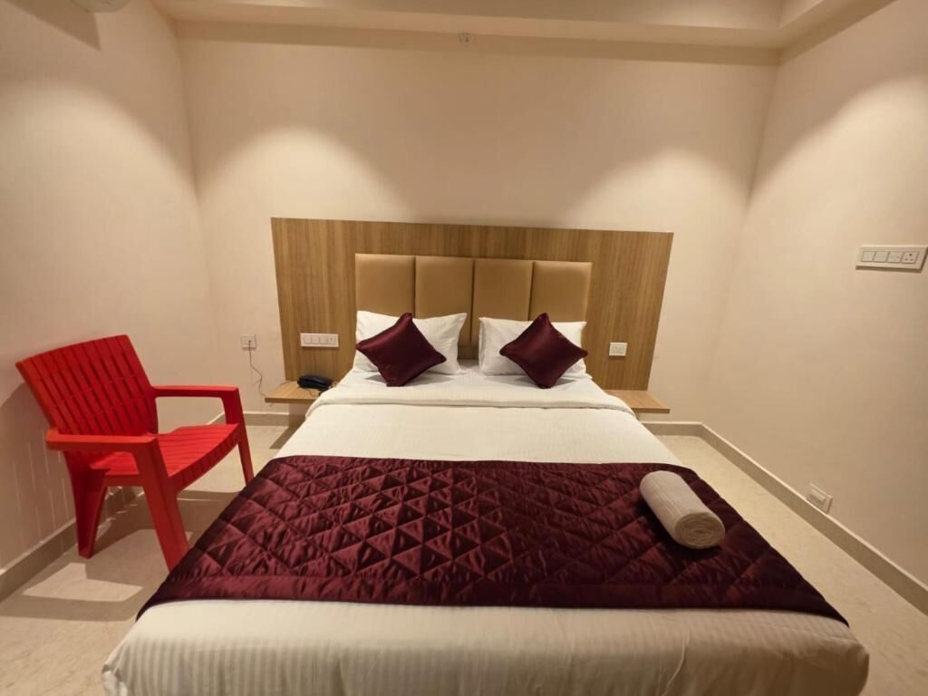 A hotel room with a bed, a red chair, and a wooden headboard.