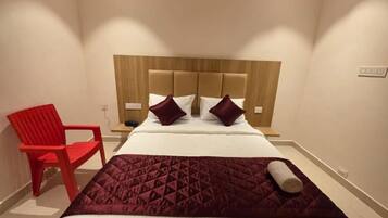 A hotel room with a bed, a red chair, and a wooden headboard.