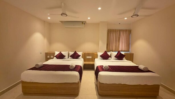 Habitación de hotel con dos camas, ventilador de techo, aire acondicionado y una ventana con cortinas.