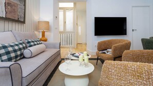 Una sala de estar con un sofá, sillones, una mesa de centro y un televisor de pantalla plana montado en la pared.