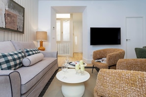 Ein Wohnzimmer mit einer Couch, Sesseln, einem Couchtisch und einem flachbildfernseher an der Wand.