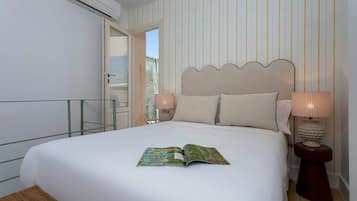 A hotel room with a bed, a nightstand with a lamp, a window with a view, and an air conditioning unit.