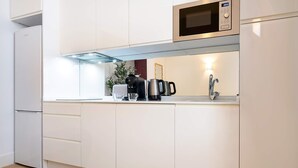Una cocina moderna con armarios blancos, microondas integrado, cafetera y lavaplatos con grifo.