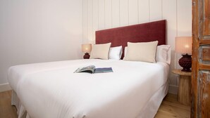 Una cama bien hecha con cabecera roja, ropa de cama blanca y una revista sobre la cama.