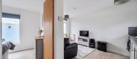 Un salon moderne avec une porte en bois, un canapé en cuir noir, un téléviseur, des haut-parleurs et un petit coin cuisine.