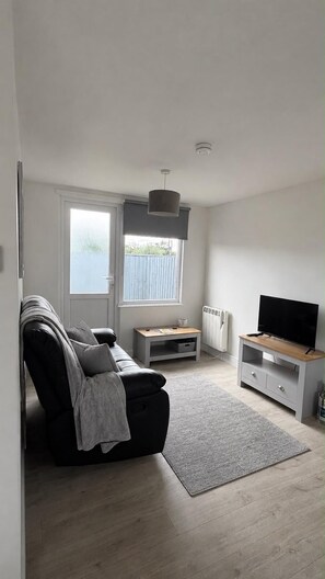 A modern living room with a sofa, a TV, a small table, and a window with a view of a fence.