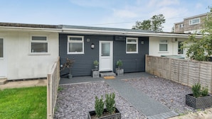 A residential property with a grey exterior, a front door, a small front yard with gravel and potted plants, and a wooden fence. - The Chalet Self Contained With Patio (Bridport)