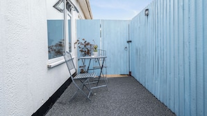 A small outdoor patio area with a metal table and chairs, a potted plant, and a blue fence. - The Chalet Self Contained With Patio (Bridport)