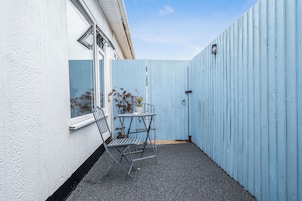 A small outdoor patio area with a metal table and chairs, a potted plant, and a blue fence.