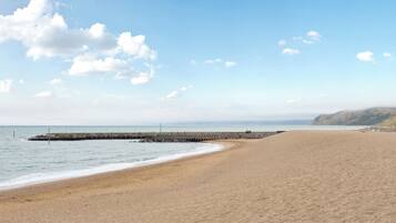 A wide sandy beach with a rocky breakwater extending into the sea, under a clear sky.