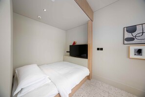 A bedroom with a single bed, a television on a shelf, and a framed picture on the wall.