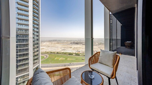 A balcony with wicker furniture, a glass table, and a view of a cityscape. - Furnished Business Bay Studio w Balcony (Dubai)