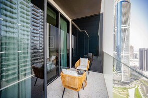 A balcony with a glass wall, wicker furniture, and a view of a tall building. - Furnished Business Bay Studio w Balcony (Dubai)