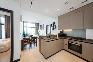A modern kitchen with a central island, a dining area with a table and chairs, and a view of the city through large windows. - Modern 2BR Retreat Near Downtown Dubai (Dubai)