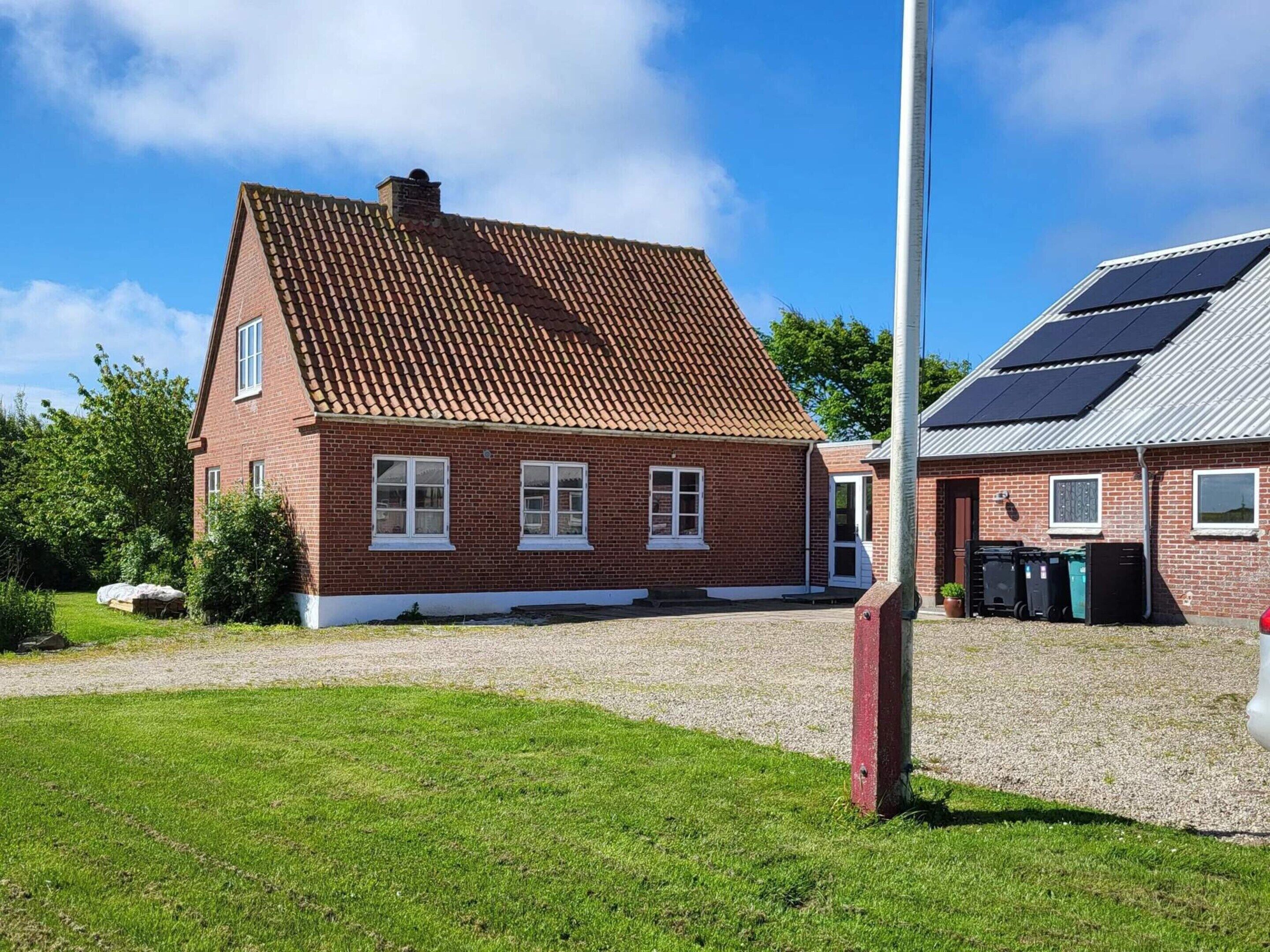 A red brick house with a tiled roof, a gravel driveway, and a solar panel installation on the adjacent building.