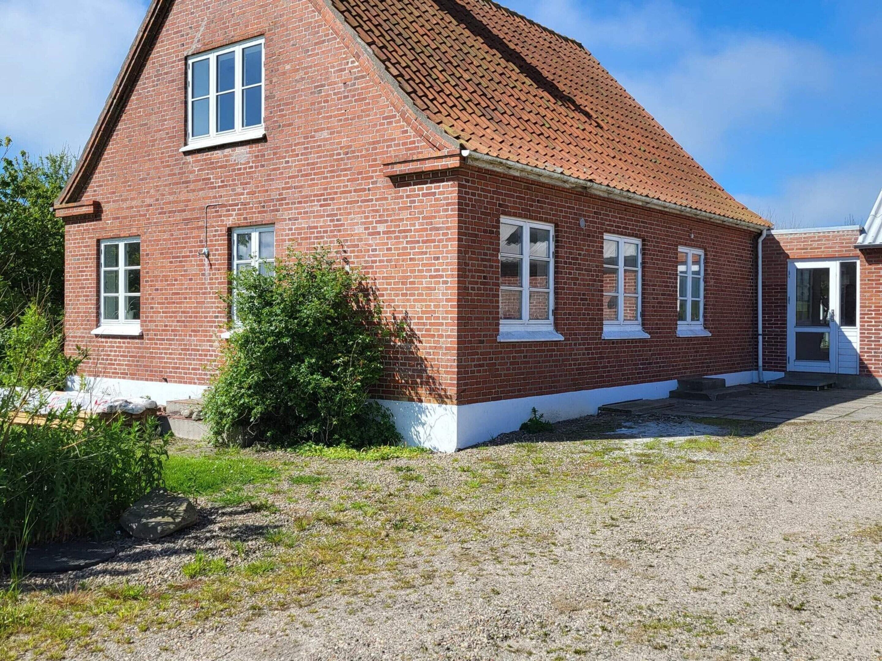 A red brick building with a pitched roof, white window frames, and a gravel driveway.