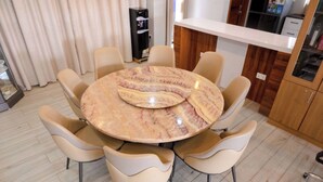 Ein runder Esstisch mit sechs Stühlen, ein Kühlschrank und eine Küchenzeile im Hintergrund.