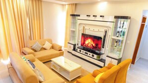 Ein Wohnzimmer mit einer Sofagarnitur, einem Couchtisch, einem Kamin und einer Vitrine mit Flaschen.