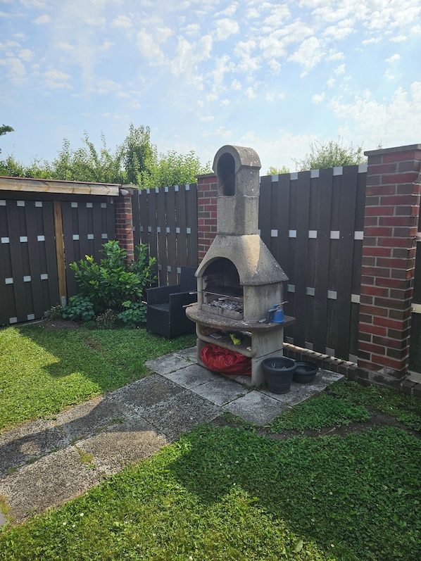 Patio con horno de piedra, cerca de madera y pared de ladrillo.