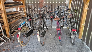 Un espace de stationnement pour vélos abrité, comprenant plusieurs vélos et des étagères de rangement en bois.