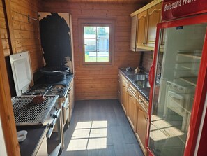 Een kleine keuken met houten wanden, een raam, een fornuis en een koelkast.