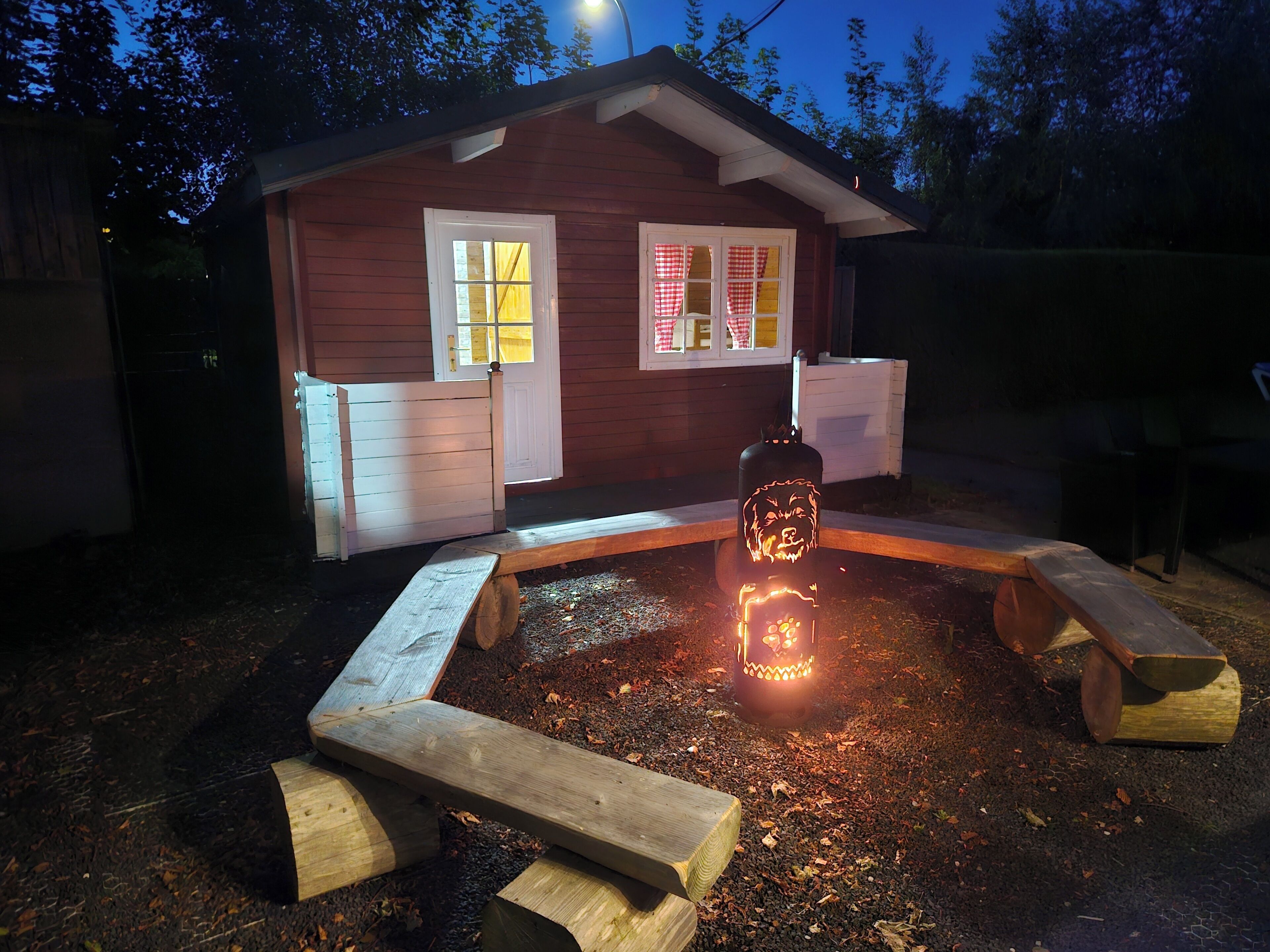 Een houten vakantiehuis met veranda, een bankje en een brandende lantaarn.
