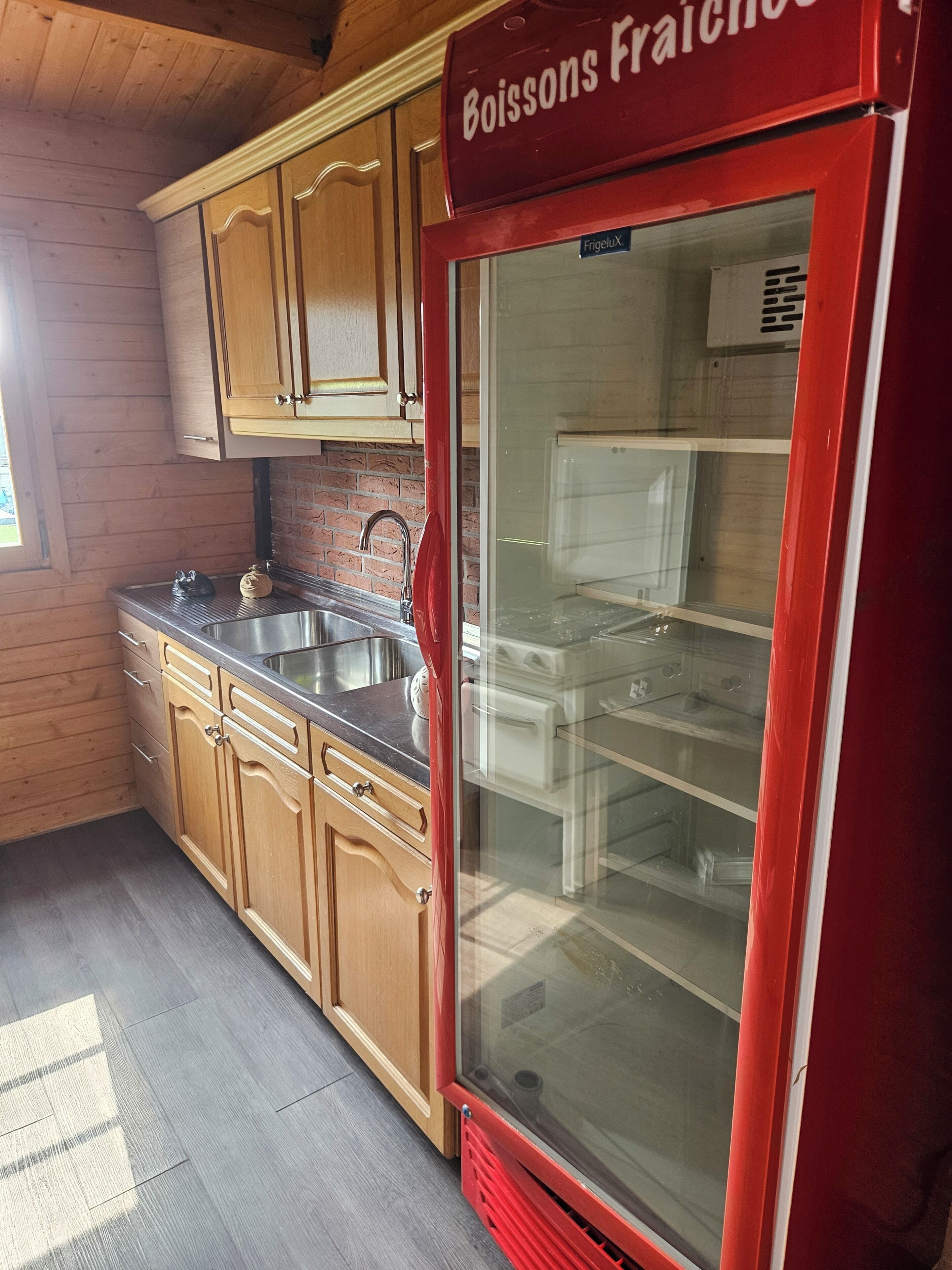 A kitchen with wooden cabinets, a stainless steel sink, and a red refrigerator.