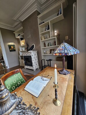 Ein Zimmer mit Kamin, Bücherregalen, einem Tisch mit Kerze und einer dekorativen Lampe.