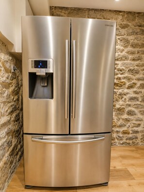A stainless steel Samsung refrigerator with a water dispenser, set against a stone wall. - Villa Margarita – Charming House Facing the Historic Ramparts | Opal Coast (Boulogne-sur-Mer)