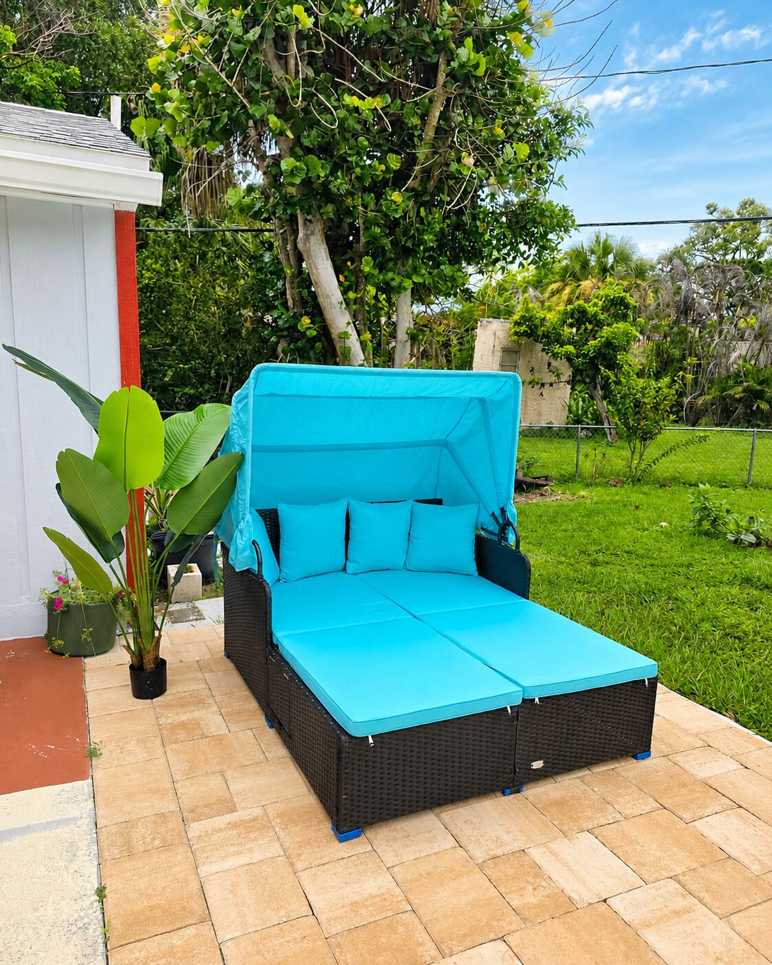 A blue outdoor sofa with cushions, positioned on a tiled patio with a green lawn and trees in the background.