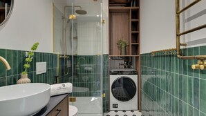 Een badkamer met een douchecabine van glas, een wastafel met een bloevas, en een ingebouwde wasmachine.