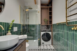 Ein Badezimmer mit Duschkabine, Waschbecken mit Blumenvase und integriertem Waschmaschinenanschluss.