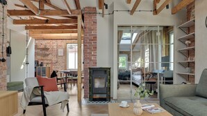 Een ruime woonkamer met zichtbare houten balken, een bakstenen muur en een groot raam.