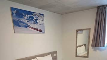 Habitación de hotel con cama, mesita de noche, espejo y un cuadro en la pared.