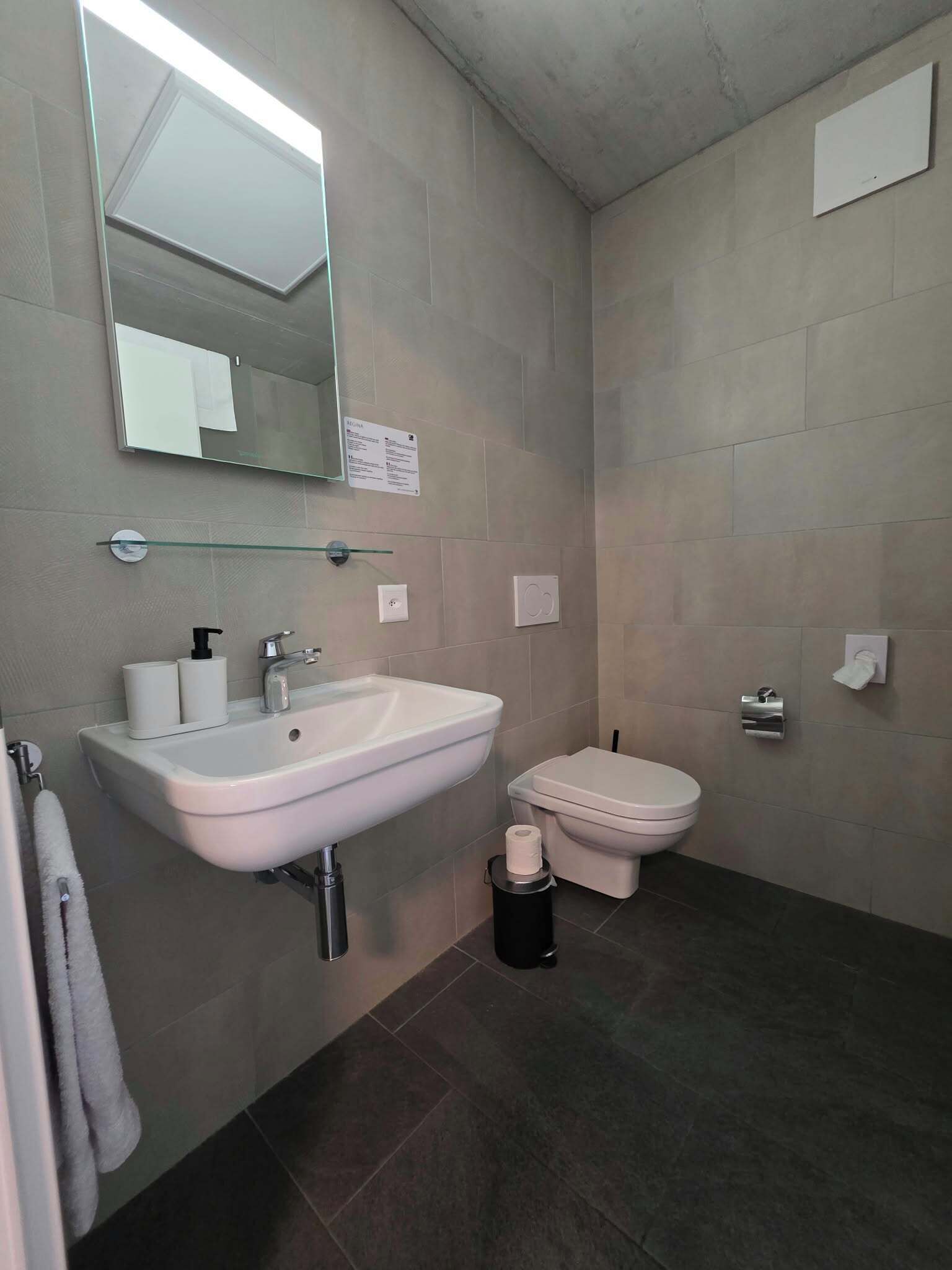 Un baño con lavamanos blanco, inodoro, espejo y repisa de vidrio.