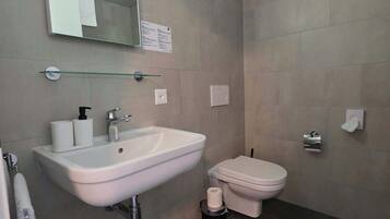 Un baño con lavamanos blanco, inodoro, espejo y repisa de vidrio.